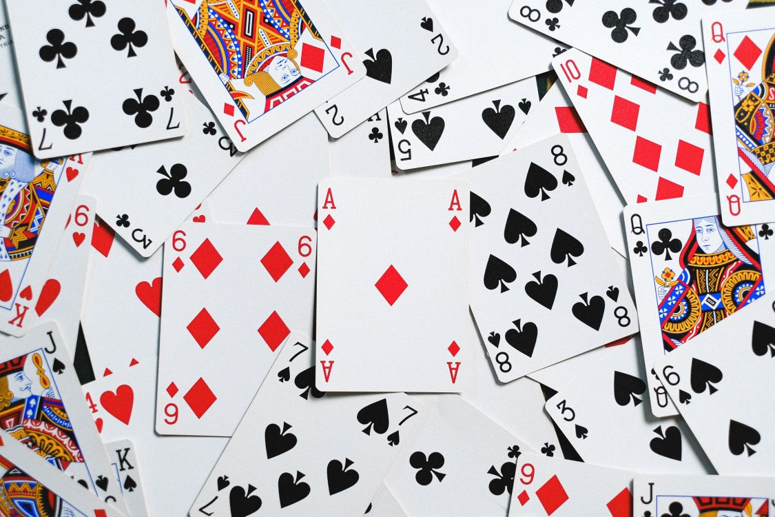 Des cartes à jouer éparpillées sur une table en bois, avec des cartes retournées et d'autres face visible, incluant des rois, des dames et des valets de différents symboles de couleur rouge et noir